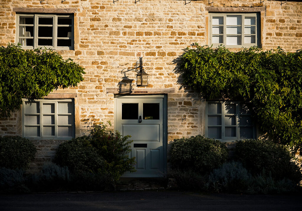 Cotswolds stone house with sage green front door and evergreen hedges