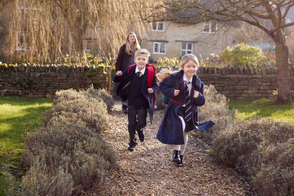 Mother Returning Home From School With Children Wearing School Uniform Running Down Path